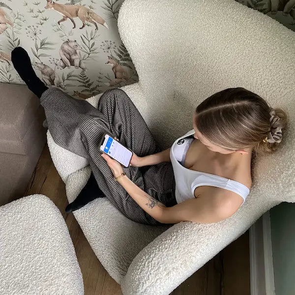 Mor der sidder i en hvid lænestol og justerer sin brystpumpe via Flow Sense appen på sin mobil.